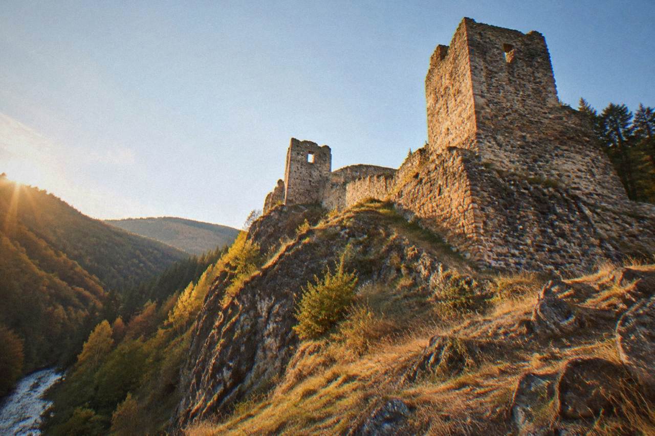 Stone ruins of a medieval hilltop fortress above forested Rhodope slopes