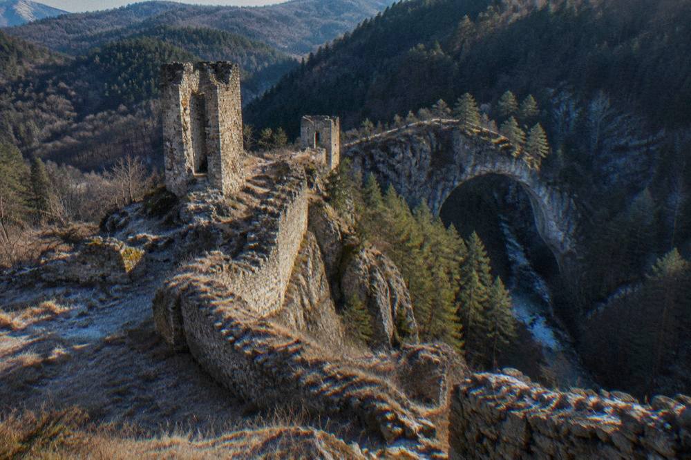 A natural stone arch bridge spanning a forested gorge in the mountains