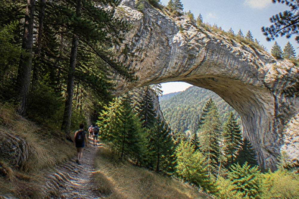 Visitors walking a forest footpath toward a large rock arch