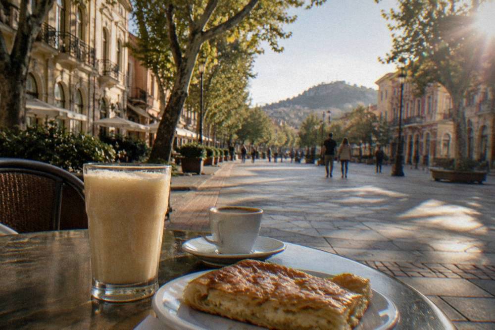 A glass of thick boza and a cup of espresso on a café table beside banitsa