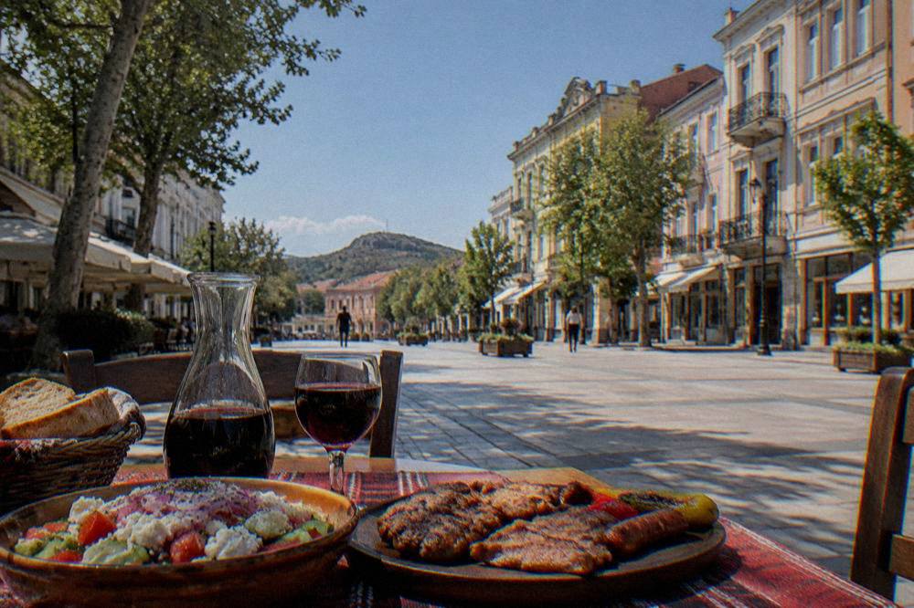 A mehana table set with shopska salad, grilled meats and a carafe of red wine