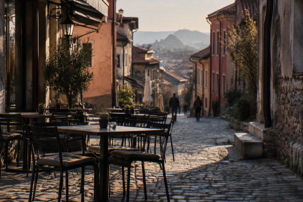 Restaurant table set on a cobbled lane in evening light with empty chairs