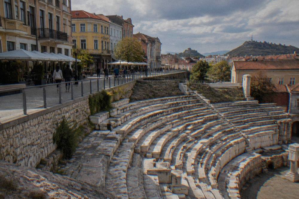 Stone seating rows of an ancient Roman stadium curve beside a modern pedestrian street