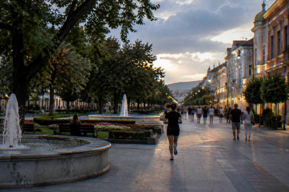People strolling on a wide pedestrian shopping street at dusk with lit facades