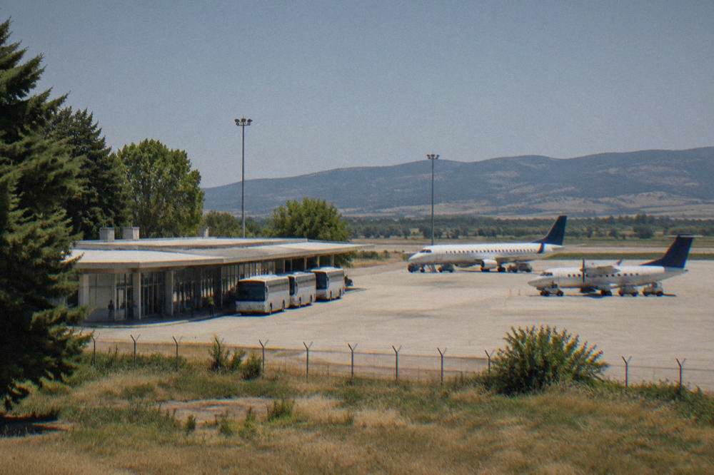 A small airport terminal building with a few parked airplanes under a clear sky