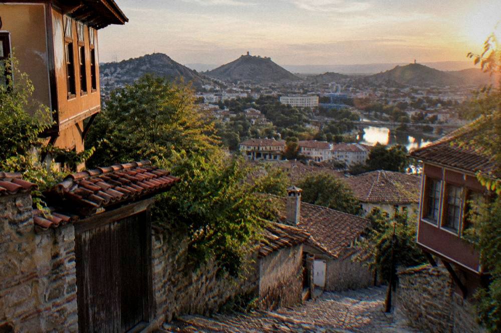 A panoramic view over the rooftops of Plovdiv from a green hilltop at sunset