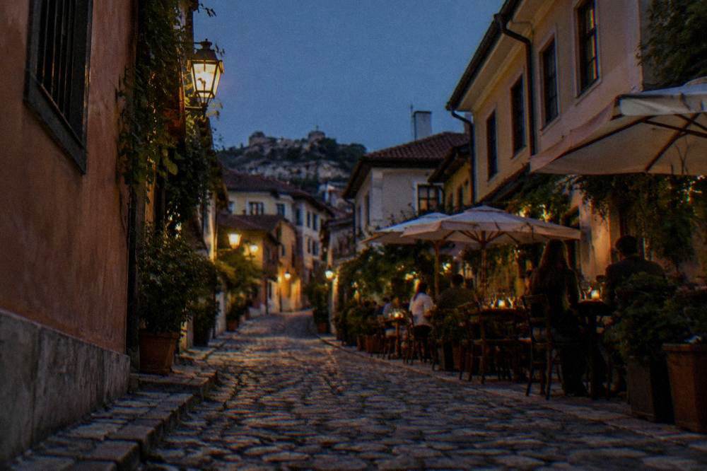 Evening diners at outdoor tables in a narrow lantern-lit street of an old quarter