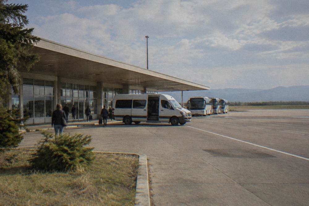 A shuttle van parked outside a small terminal waiting for arriving passengers