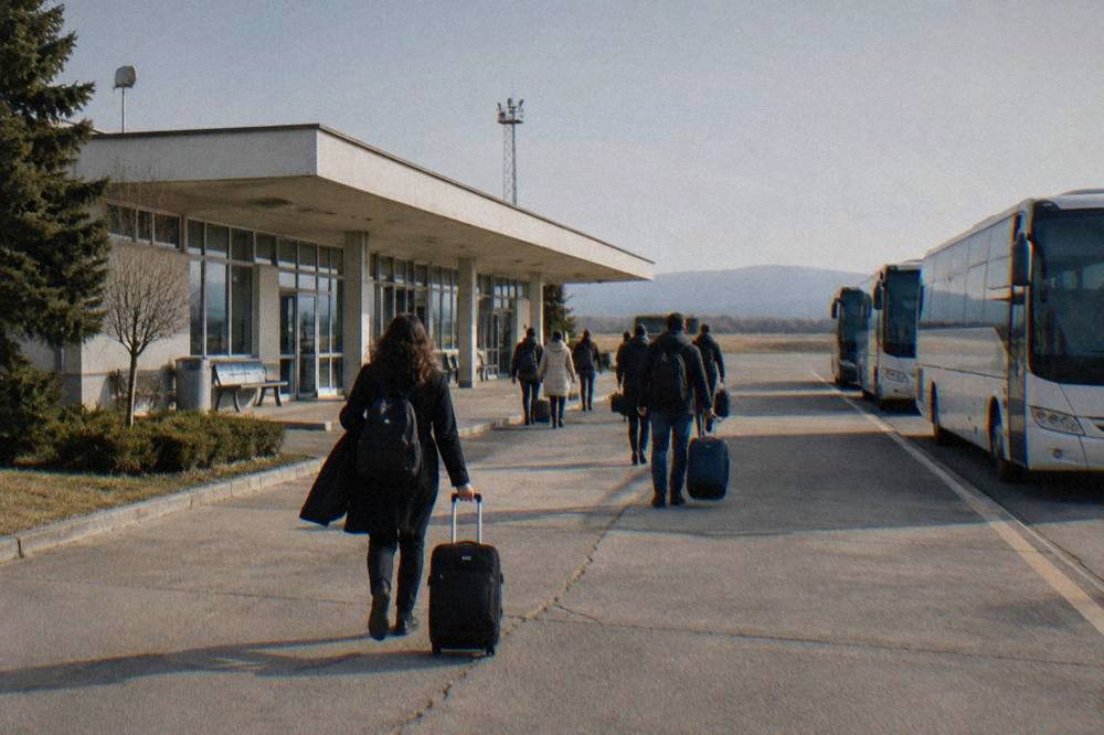 Passengers with luggage walking out of a small terminal into afternoon sun
