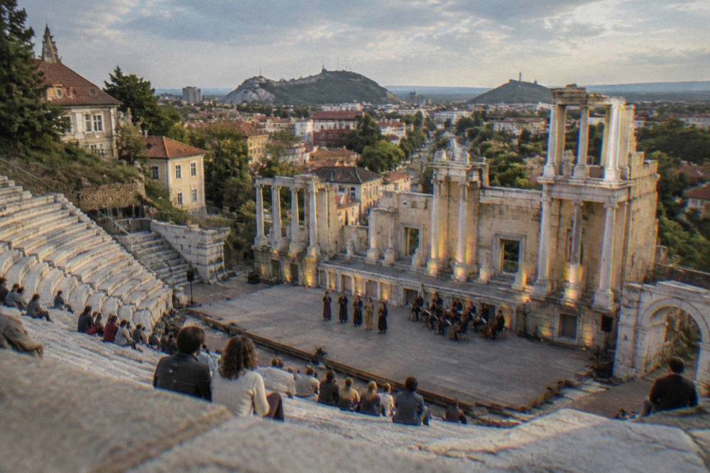 People gathered on an ancient marble theatre stage during an open-air evening performance