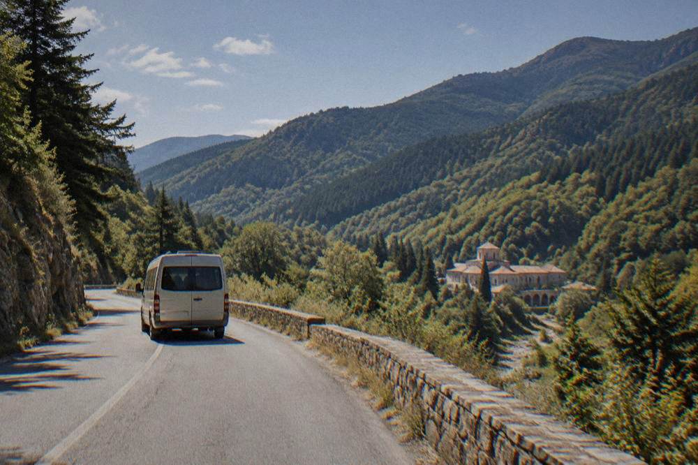A minibus winding along a road in the Rhodope mountains toward Bachkovo Monastery