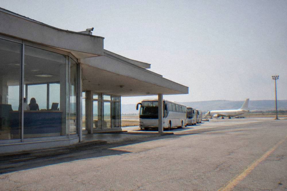 A rental car counter inside a small airport terminal with a plane visible through the window