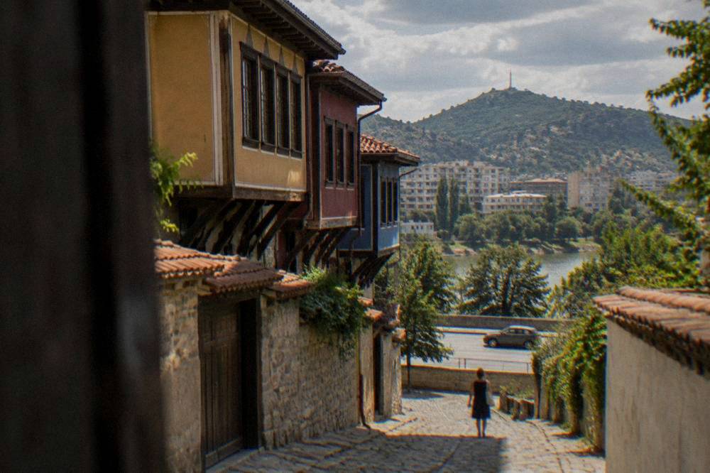 A car driving on a boulevard in Plovdiv with green hills rising behind apartment blocks