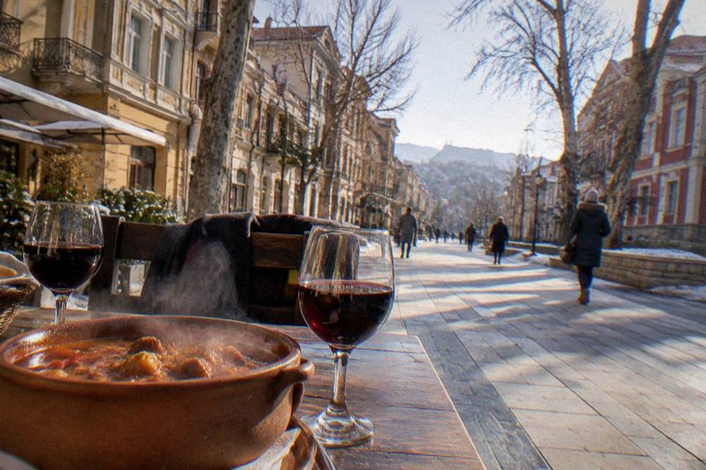 A clay pot of steaming stew and glasses of red wine on a rustic restaurant table