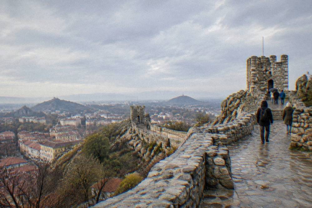 Visitors walking among the ruined walls of Nebet Tepe above the rooftops of Plovdiv