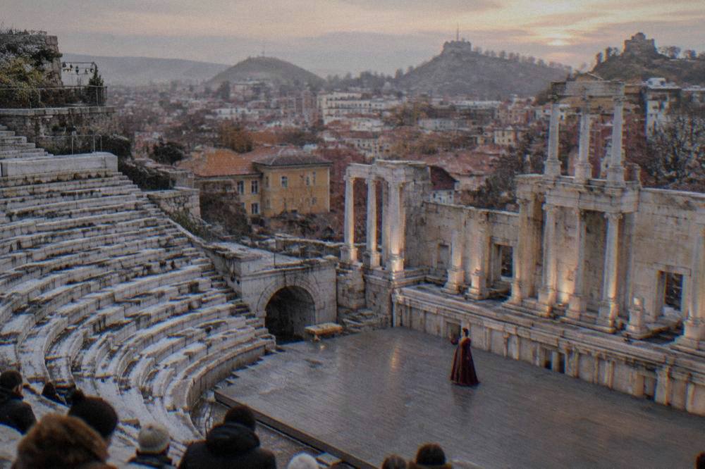 A soprano in costume performing on an ancient stone stage at dusk