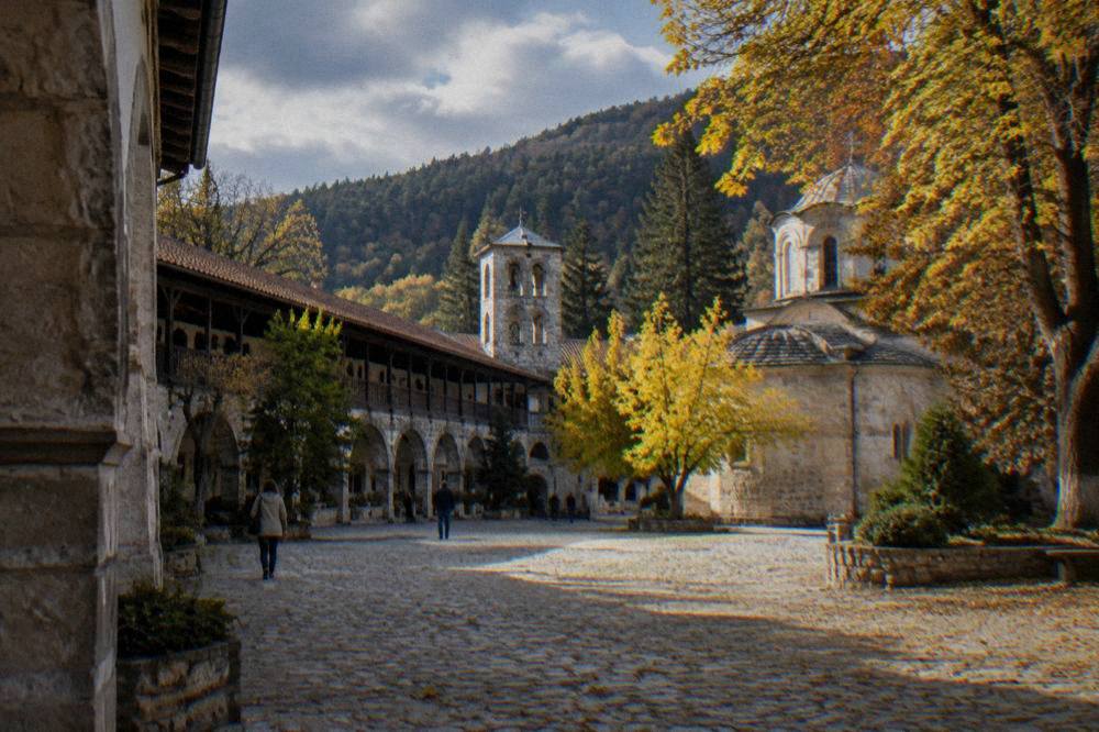 Stone arches of Bachkovo Monastery courtyard with trees turning yellow in autumn