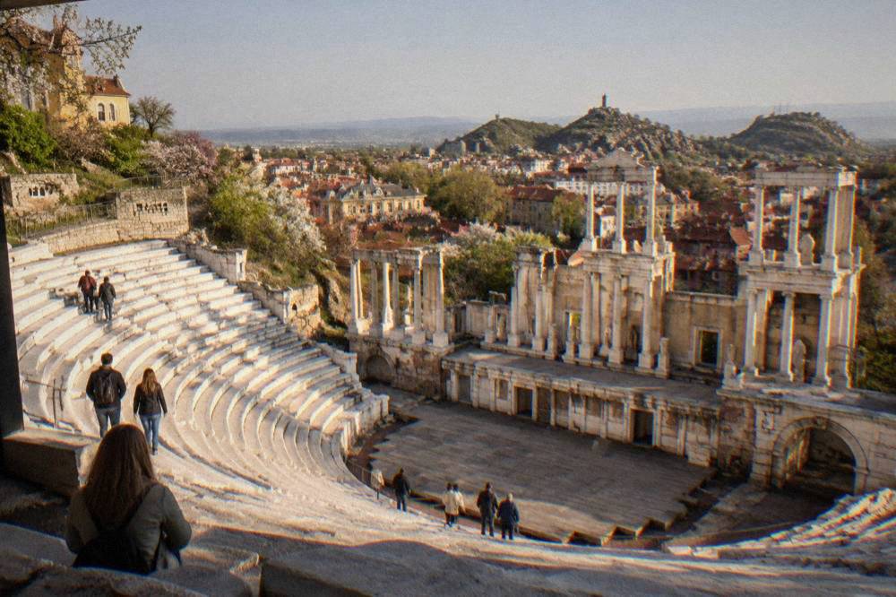 Visitors walking among marble rows of the Ancient Theatre of Philippopolis under a clear spring sky