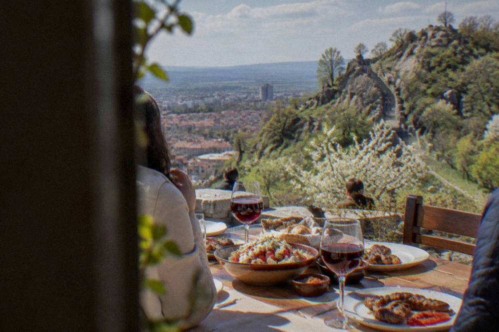 A table with shopska salad, grill dishes and glasses of red wine on a sunny terrace