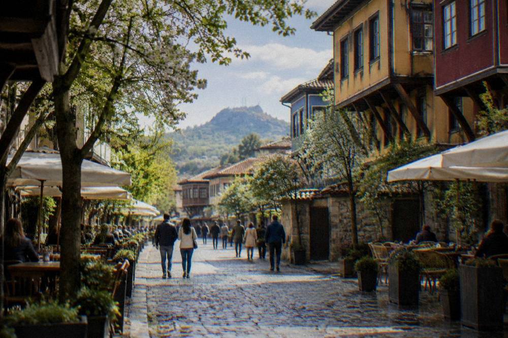People strolling on Plovdiv Main Street under green trees with cafe terraces on both sides