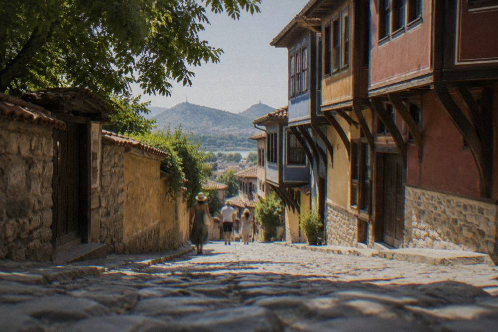 A shaded cobbled street in the Plovdiv Old Town with overhanging balconies in bright afternoon light