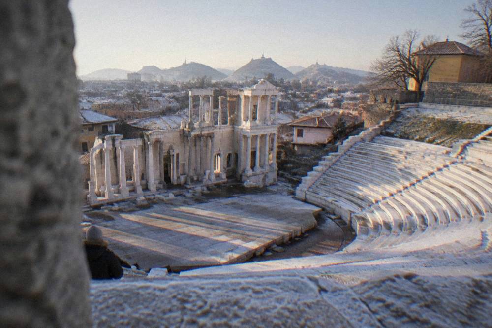Empty marble seating rows of the Ancient Theatre with the city rooftops beyond under a pale sky