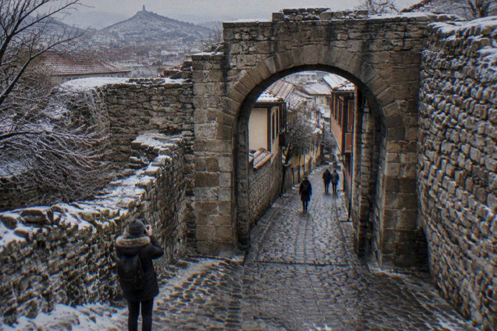 A visitor in a winter coat photographing the Hisar Kapia gate with frost on the surrounding stone walls