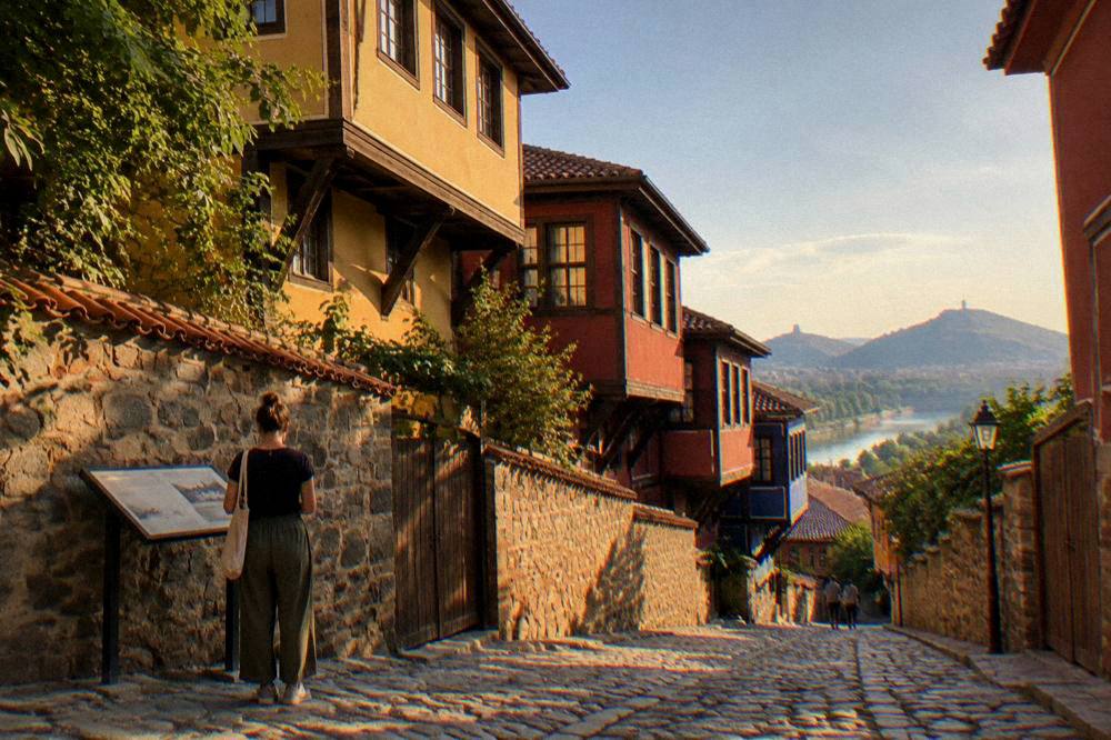 A visitor reading a bilingual information plaque beside an old stone building in Plovdiv