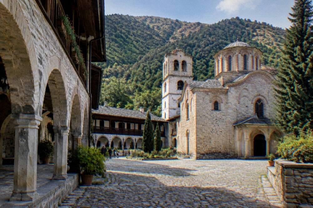 Stone arches of Bachkovo Monastery courtyard with a mountain backdrop