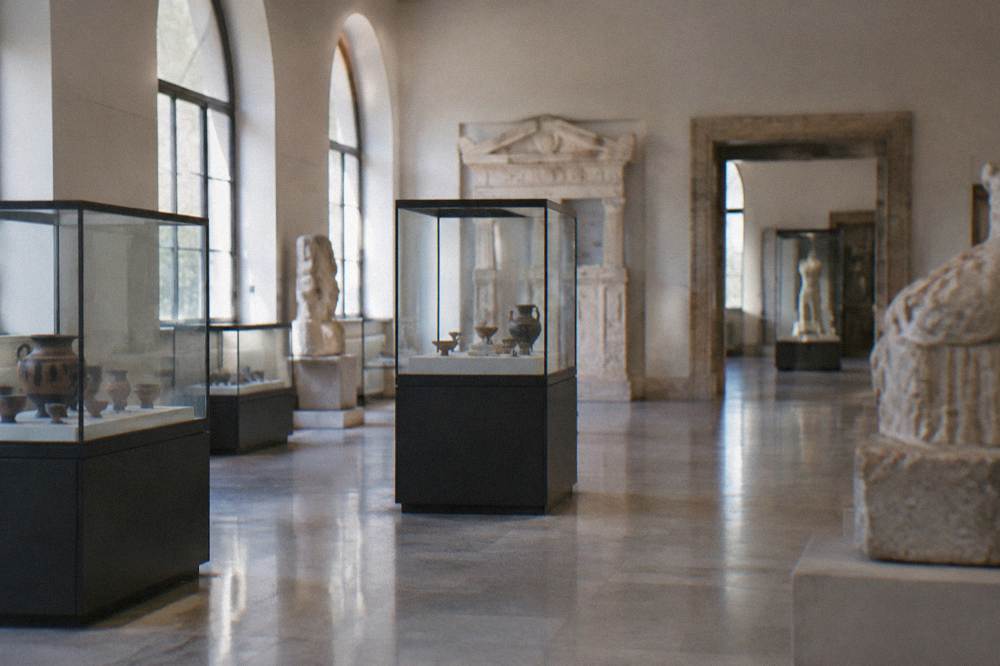 Museum interior gallery with display cases and a stone floor, empty