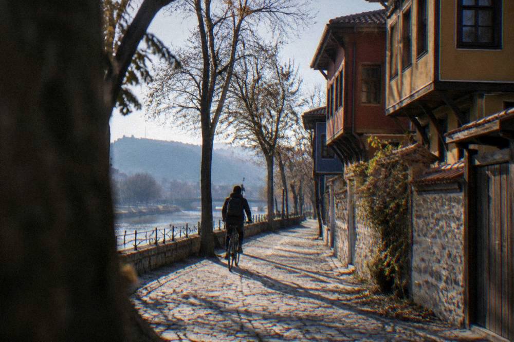 A cyclist riding along a tree-lined path beside a river in Plovdiv