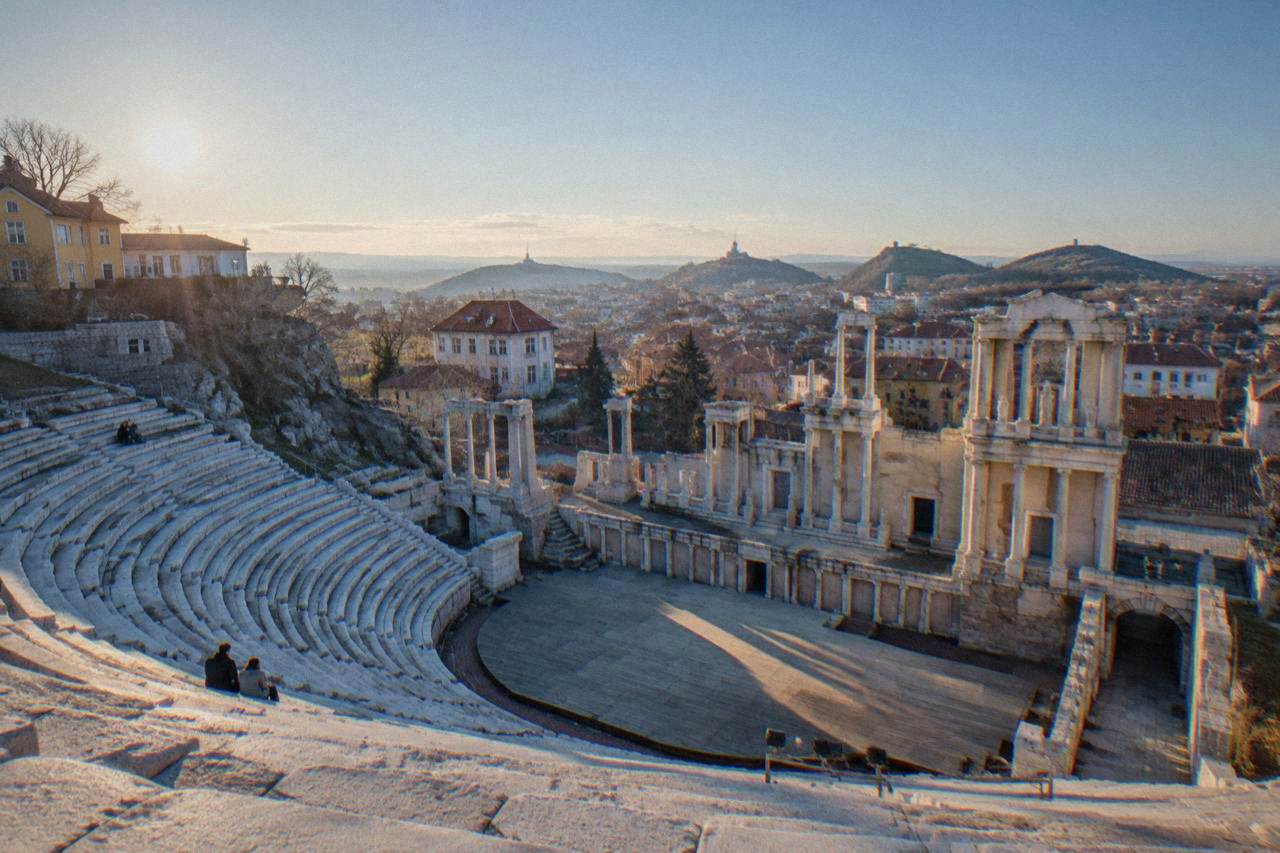 Marble rows of an ancient theatre framed by a hillside town at late afternoon