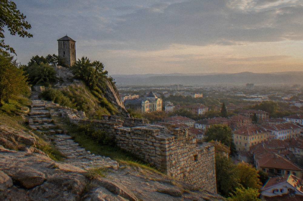 Stone fortress walls on a hilltop overlooking a dense rooftop panorama at dusk