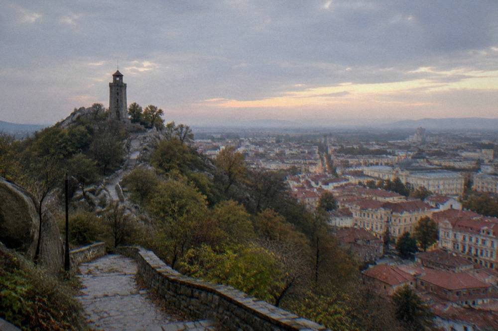 A tall hilltop monument silhouetted against a wide city spread under evening sky