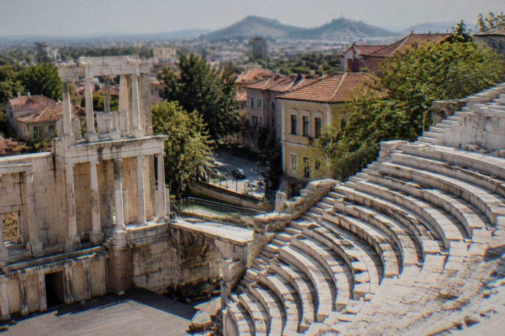 An ancient stone theatre with rows of marble seats above a modern city street