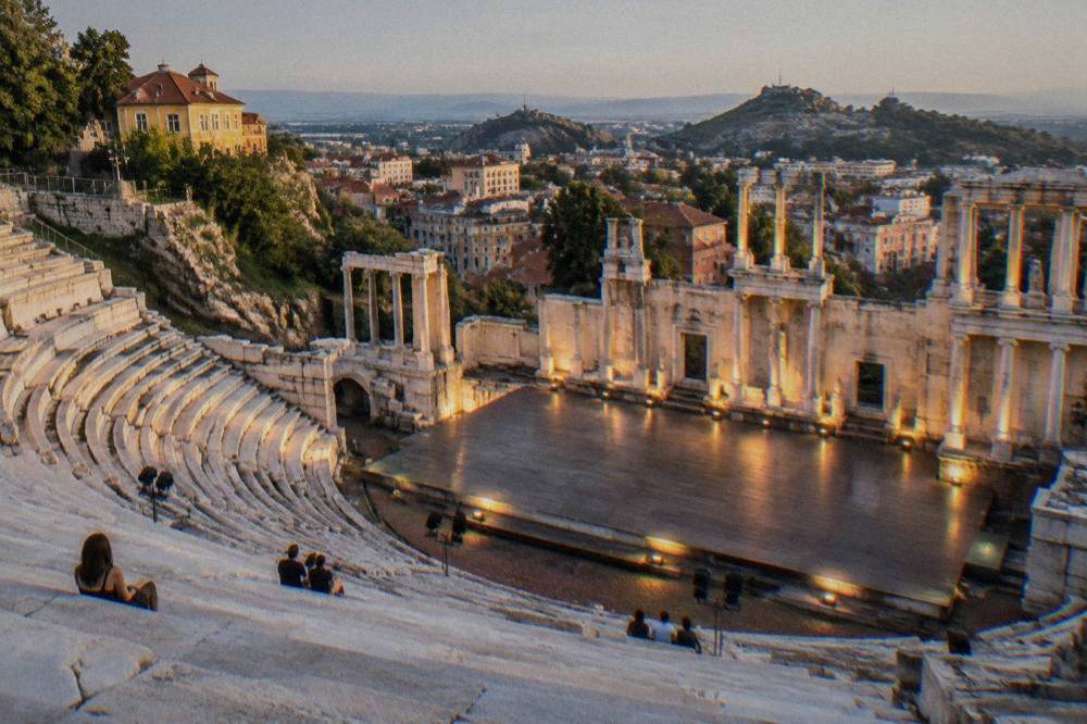 A floodlit ancient theatre stage seen from the upper marble rows before an evening performance