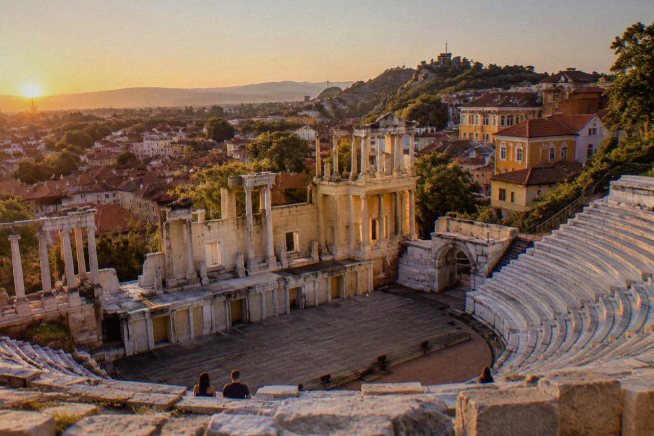 Sunlit rooftops of Plovdiv Old Town with the Ancient Theatre hill rising above red tiles under a clear sky