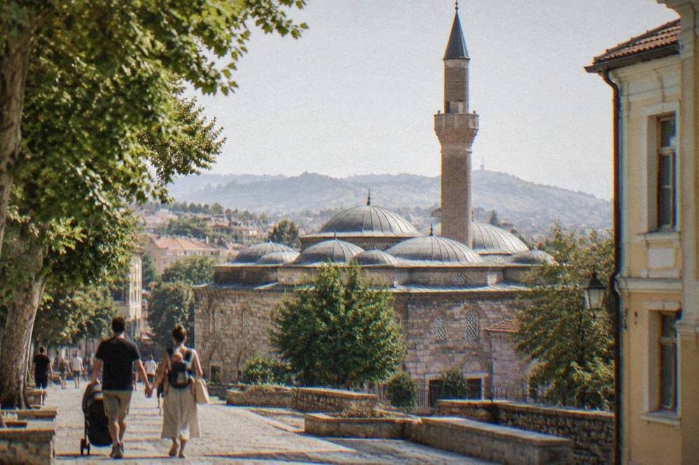 A family with a baby carrier walking past the Dzhumaya Mosque minaret in central Plovdiv