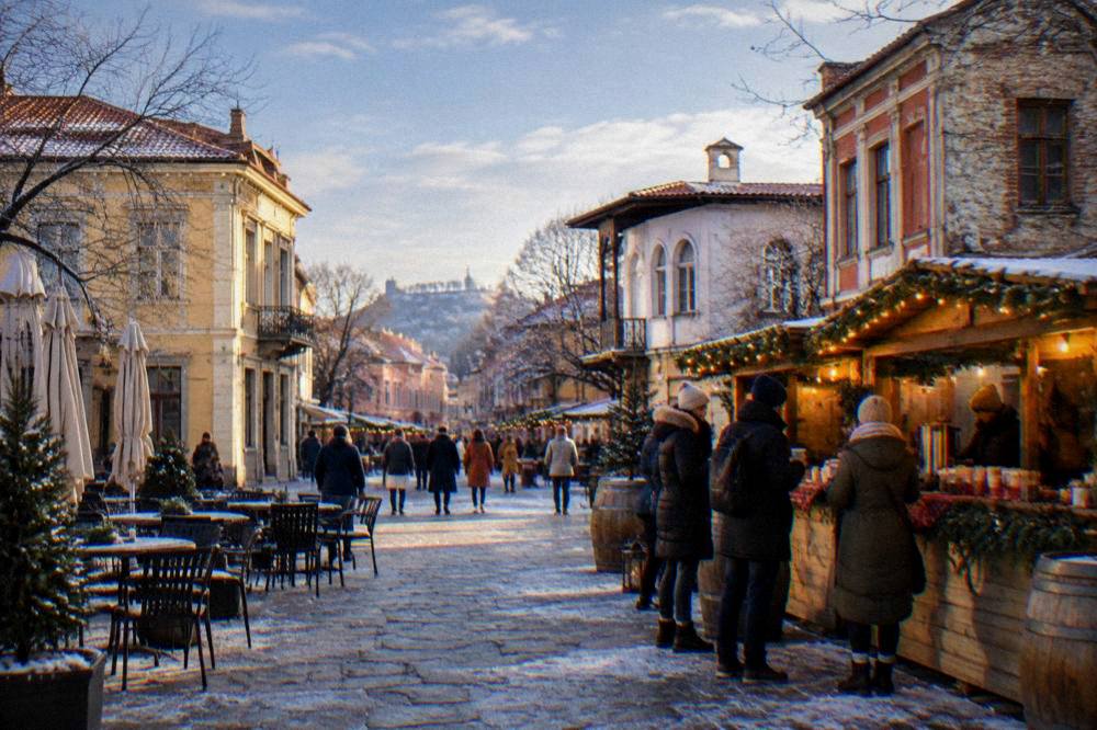 A festive outdoor winter market stall with warm lights and people in coats holding drinks