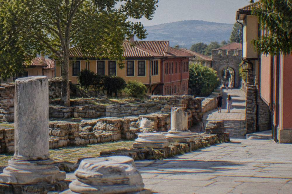 A narrow cobbled street of old houses rising toward a stone gate