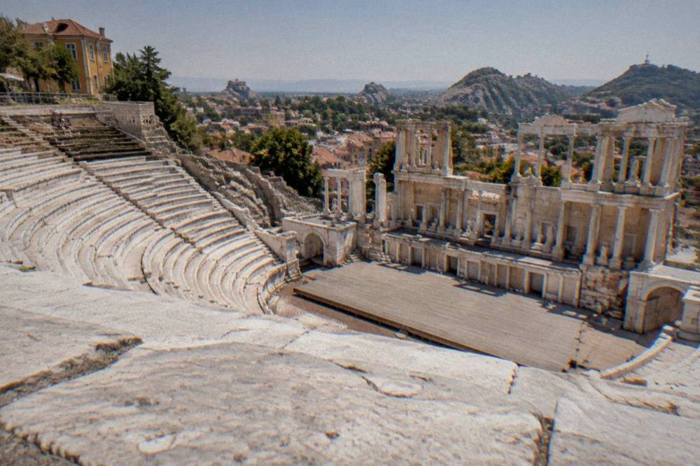 The marble seat rows of an ancient Roman theatre on a hillside above a city