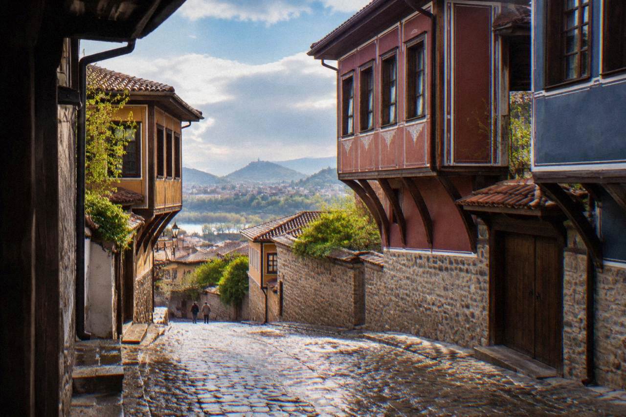 A cobblestone street in Plovdiv Old Town glistening with rain, revival-era houses with overhanging eaves on either side