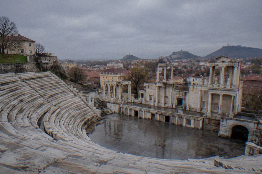The wet marble seat rows of the Ancient Theatre of Philippopolis under a grey sky, empty between showers