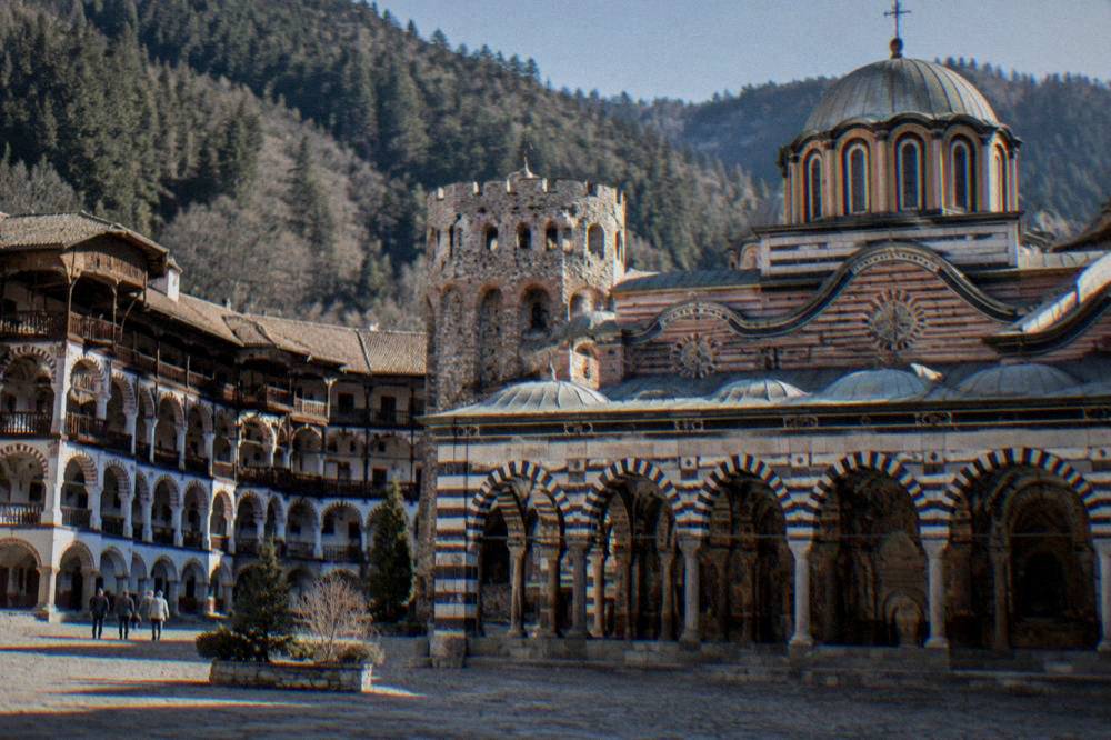 A mountain monastery courtyard with arched balconies and a striped stone church facade