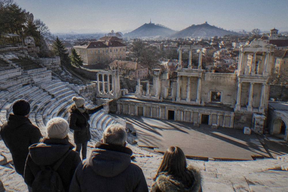 Guide speaking to a small group beside the marble seats of the Ancient Theatre of Philippopolis