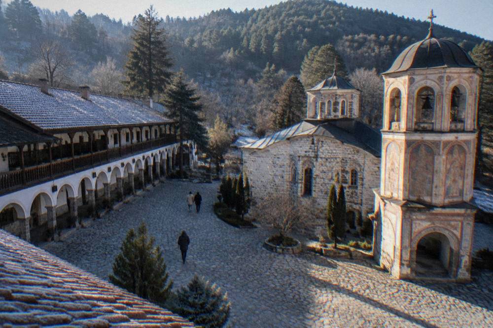 A courtyard of a Bulgarian monastery with an arcaded gallery and a painted church tower.